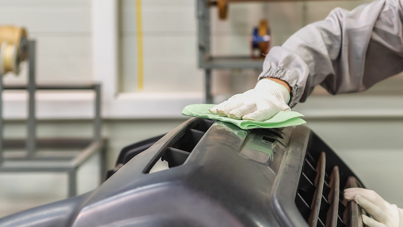 Gloved hand wiping an unpainted bumper with a tack cloth in a paintshop